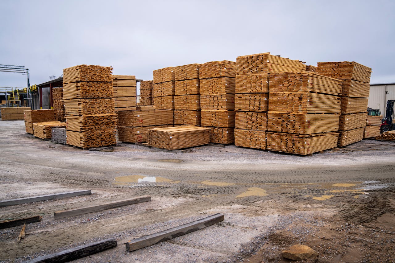 who-we-are Piles of wooden planks prepared for distribution in an outdoor industrial site.