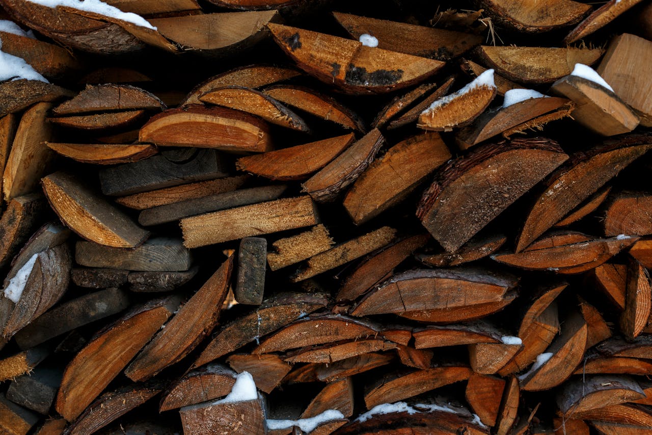 Close-up of stacked firewood with snow, showcasing natural textures and tones for rustic warmth.